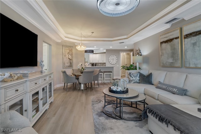 living room featuring a chandelier, light wood-type flooring, a raised ceiling, and crown molding