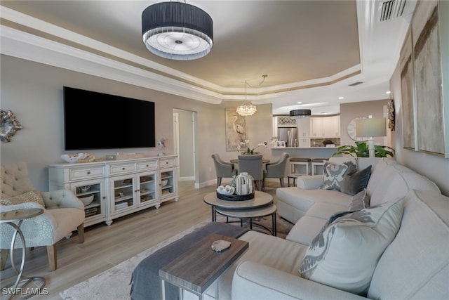 living room featuring a raised ceiling, light hardwood / wood-style flooring, ornamental molding, and an inviting chandelier