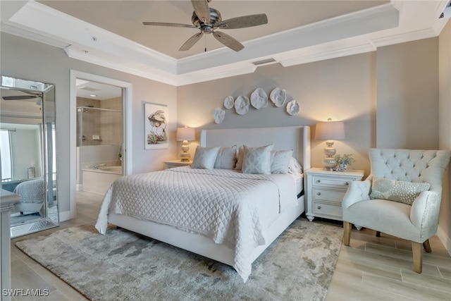 bedroom featuring light wood-type flooring, ensuite bath, ornamental molding, a raised ceiling, and ceiling fan