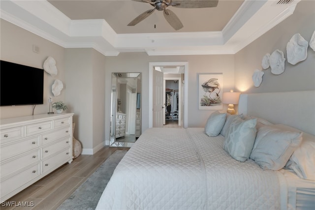 bedroom featuring ceiling fan, a walk in closet, light wood-type flooring, and crown molding