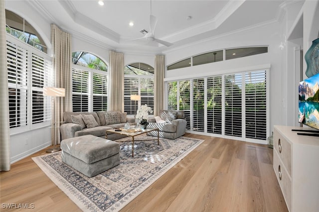 living room with a raised ceiling, ceiling fan, crown molding, and light hardwood / wood-style floors