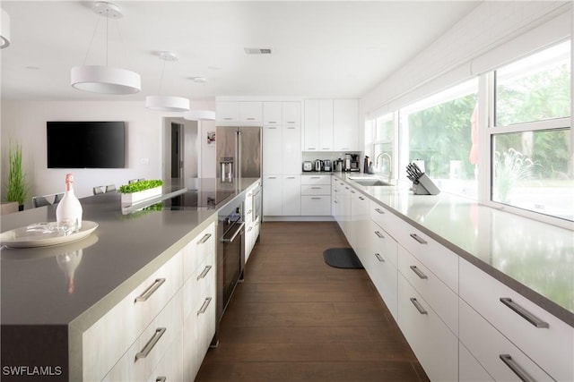 kitchen with dark wood-type flooring, white cabinets, a sink, decorative light fixtures, and stainless steel appliances