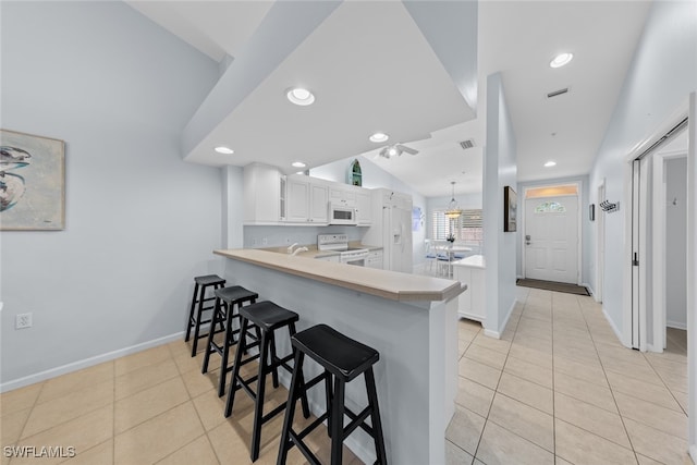 kitchen with white appliances, a kitchen breakfast bar, kitchen peninsula, light tile patterned floors, and white cabinetry