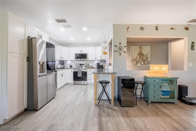 kitchen with white cabinets, light hardwood / wood-style floors, a kitchen bar, kitchen peninsula, and stainless steel appliances