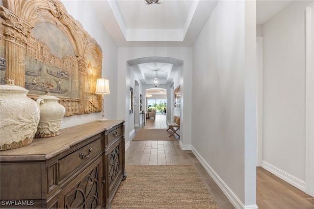 hall with hardwood / wood-style floors and a raised ceiling