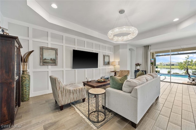 living room with light wood-type flooring, an inviting chandelier, and a raised ceiling