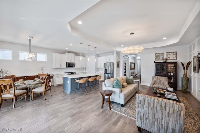 living room featuring light hardwood / wood-style floors, a raised ceiling, sink, and a chandelier