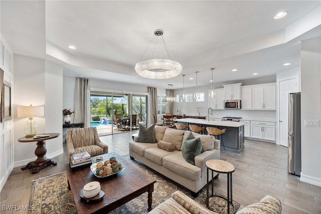 living room with an inviting chandelier, light wood-type flooring, and a tray ceiling