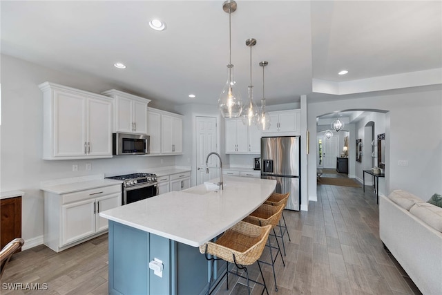 kitchen with a breakfast bar, stainless steel appliances, pendant lighting, light hardwood / wood-style flooring, and white cabinets