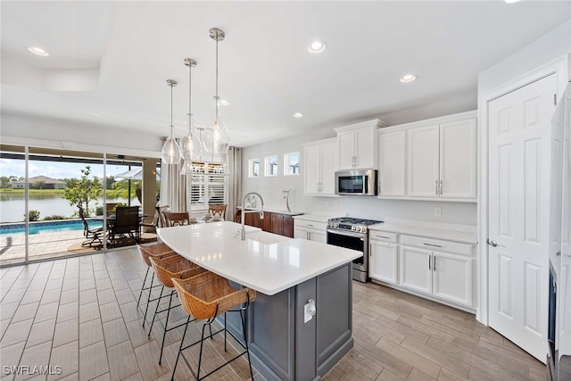 kitchen with white cabinetry, a water view, stainless steel appliances, and decorative light fixtures