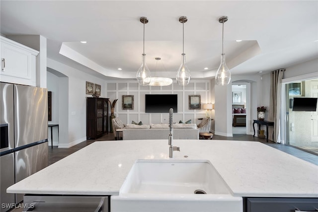 kitchen with sink, stainless steel appliances, decorative light fixtures, a tray ceiling, and a center island with sink