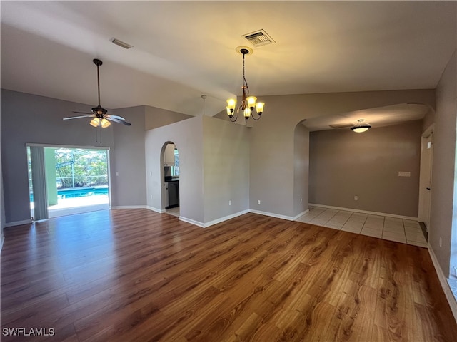 empty room featuring hardwood / wood-style floors, ceiling fan with notable chandelier, and lofted ceiling