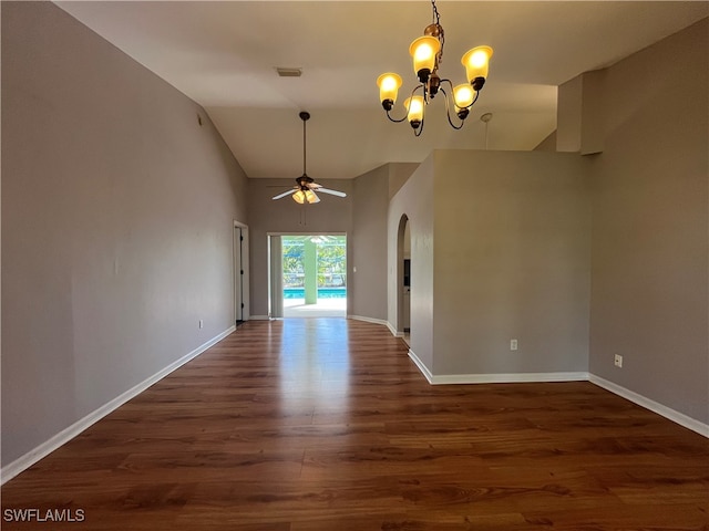 spare room featuring ceiling fan with notable chandelier, dark wood-type flooring, and lofted ceiling