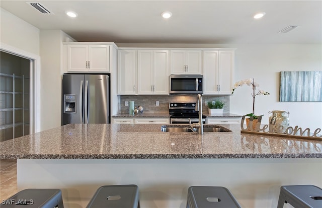 kitchen with stainless steel appliances, white cabinets, sink, a breakfast bar area, and stone countertops