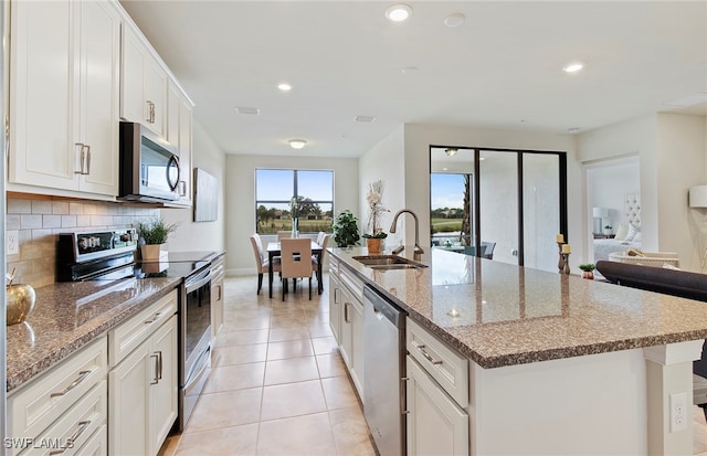 kitchen with stainless steel appliances, white cabinets, decorative backsplash, sink, and an island with sink