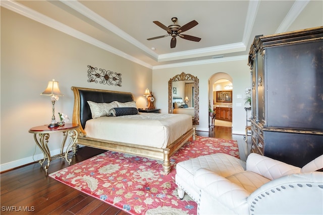 bedroom featuring ensuite bath, ornamental molding, a tray ceiling, ceiling fan, and dark hardwood / wood-style floors