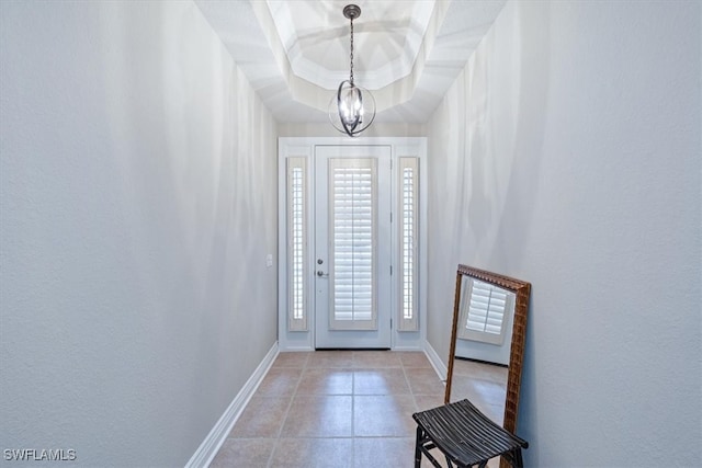 foyer with a chandelier, light tile patterned floors, and a raised ceiling