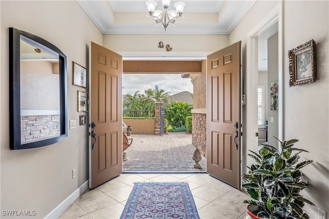 tiled foyer with ornamental molding, a chandelier, and a tray ceiling