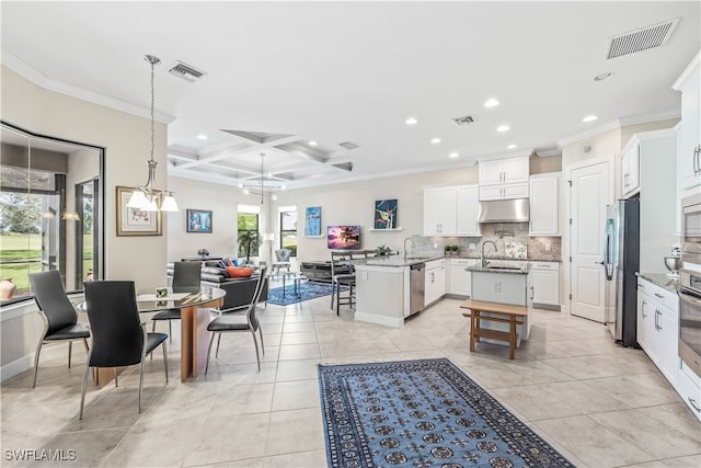 kitchen featuring appliances with stainless steel finishes, a wealth of natural light, an island with sink, and coffered ceiling