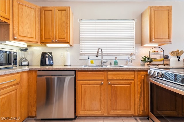 kitchen with appliances with stainless steel finishes, backsplash, light tile patterned floors, and sink