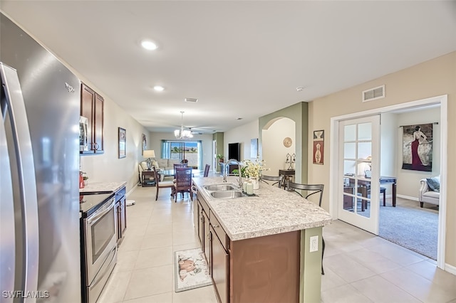 kitchen featuring a center island with sink, sink, appliances with stainless steel finishes, light tile patterned floors, and a chandelier