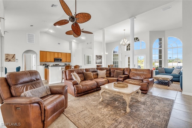 tiled living room featuring ceiling fan with notable chandelier and high vaulted ceiling