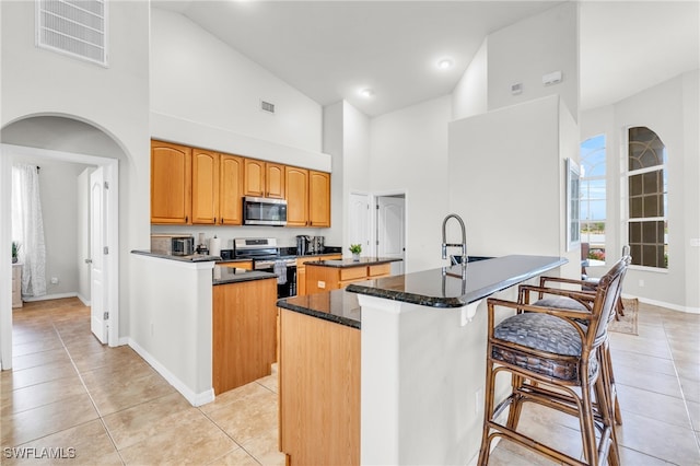 kitchen featuring sink, light tile patterned floors, an island with sink, stainless steel appliances, and a high ceiling