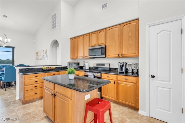 kitchen featuring a kitchen island, appliances with stainless steel finishes, a breakfast bar, decorative light fixtures, and dark stone countertops