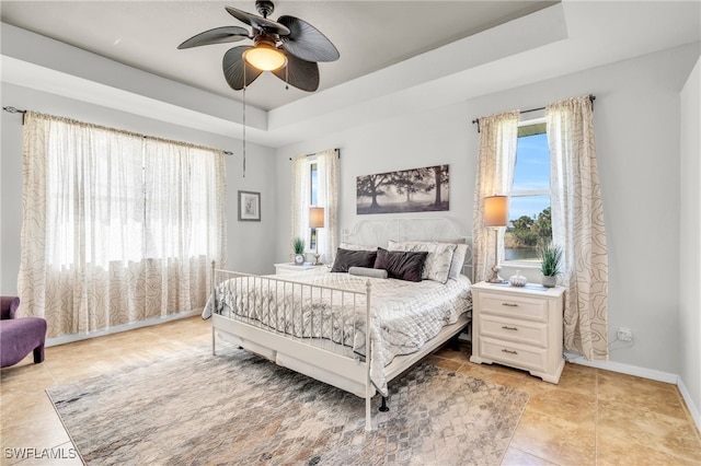 tiled bedroom featuring a raised ceiling, multiple windows, and ceiling fan