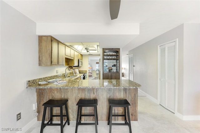 kitchen featuring light stone counters, appliances with stainless steel finishes, sink, a breakfast bar, and kitchen peninsula