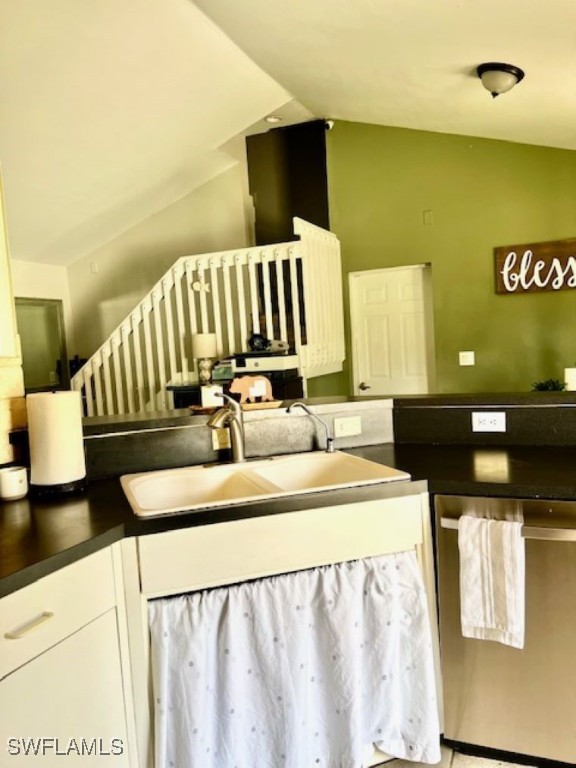 kitchen featuring stainless steel dishwasher, white cabinetry, sink, and lofted ceiling