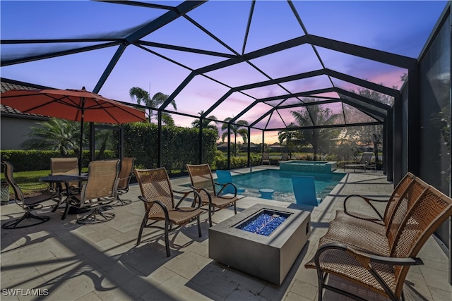 pool at dusk with glass enclosure, a patio area, and a fire pit