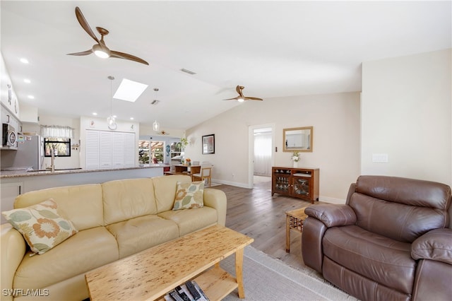 living room featuring sink, lofted ceiling with skylight, light hardwood / wood-style floors, and ceiling fan