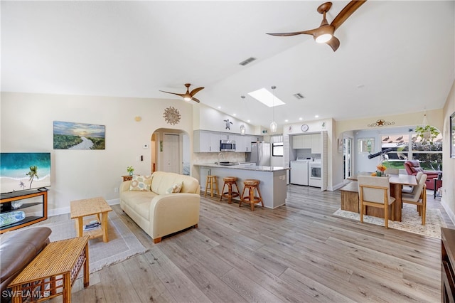 living room featuring lofted ceiling with skylight, washer and dryer, sink, ceiling fan, and light wood-type flooring