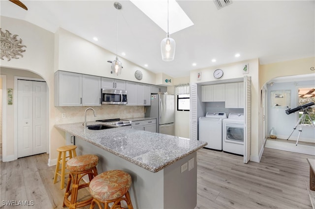 kitchen with appliances with stainless steel finishes, a kitchen breakfast bar, kitchen peninsula, independent washer and dryer, and light stone countertops