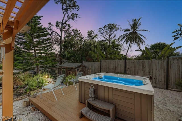 pool at dusk with a wooden deck and a hot tub