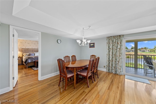 dining space with a notable chandelier, a raised ceiling, light wood-type flooring, and a water view