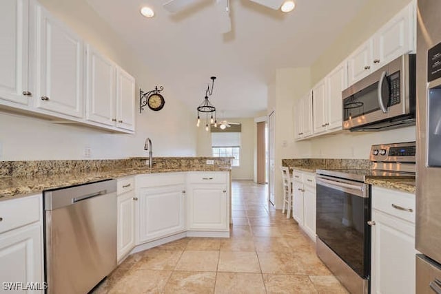 kitchen featuring white cabinets, appliances with stainless steel finishes, a peninsula, light stone countertops, and a sink