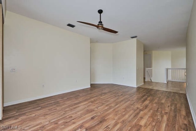 empty room with a ceiling fan, visible vents, baseboards, and wood finished floors