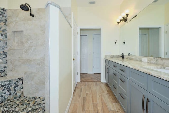 bathroom with double vanity, a sink, tiled shower, and wood finished floors