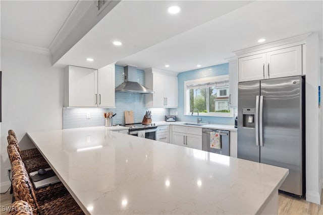 kitchen with kitchen peninsula, stainless steel appliances, white cabinetry, and wall chimney range hood