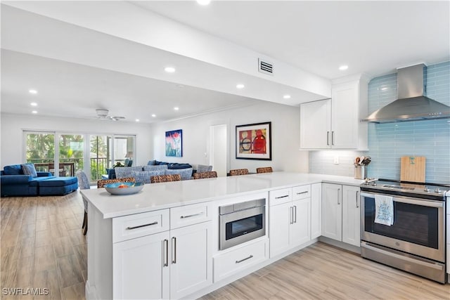 kitchen featuring appliances with stainless steel finishes, wall chimney exhaust hood, white cabinetry, backsplash, and kitchen peninsula