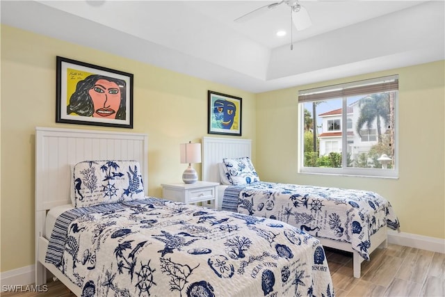 bedroom featuring ceiling fan, light hardwood / wood-style floors, and a tray ceiling