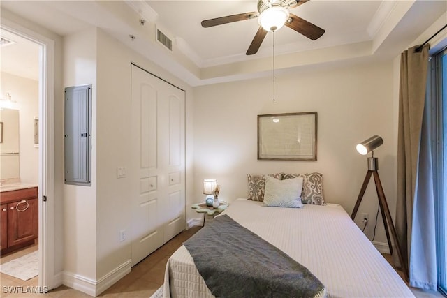 bedroom featuring connected bathroom, ceiling fan, a raised ceiling, electric panel, and a closet