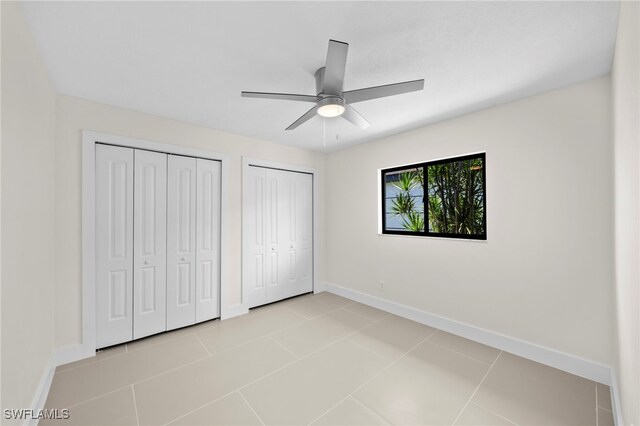 unfurnished bedroom with ceiling fan, light tile patterned flooring, and two closets