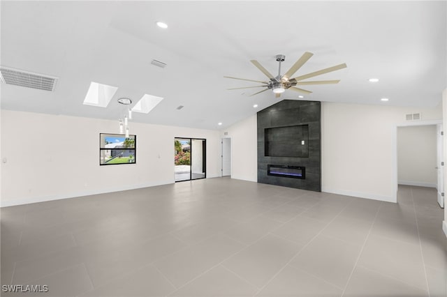 unfurnished living room with ceiling fan, light tile patterned flooring, lofted ceiling with skylight, and a tiled fireplace