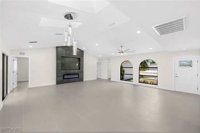 unfurnished living room featuring a tiled fireplace, ceiling fan, light tile patterned flooring, and lofted ceiling with skylight