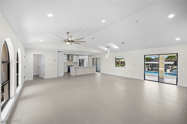 unfurnished living room with lofted ceiling with skylight, light tile patterned flooring, and ceiling fan