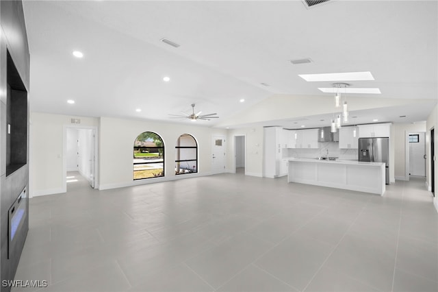 unfurnished living room featuring vaulted ceiling with skylight, ceiling fan, and light tile patterned floors