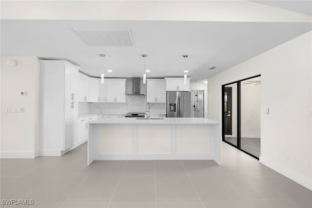 kitchen featuring white cabinets, stainless steel fridge, a center island with sink, and wall chimney exhaust hood